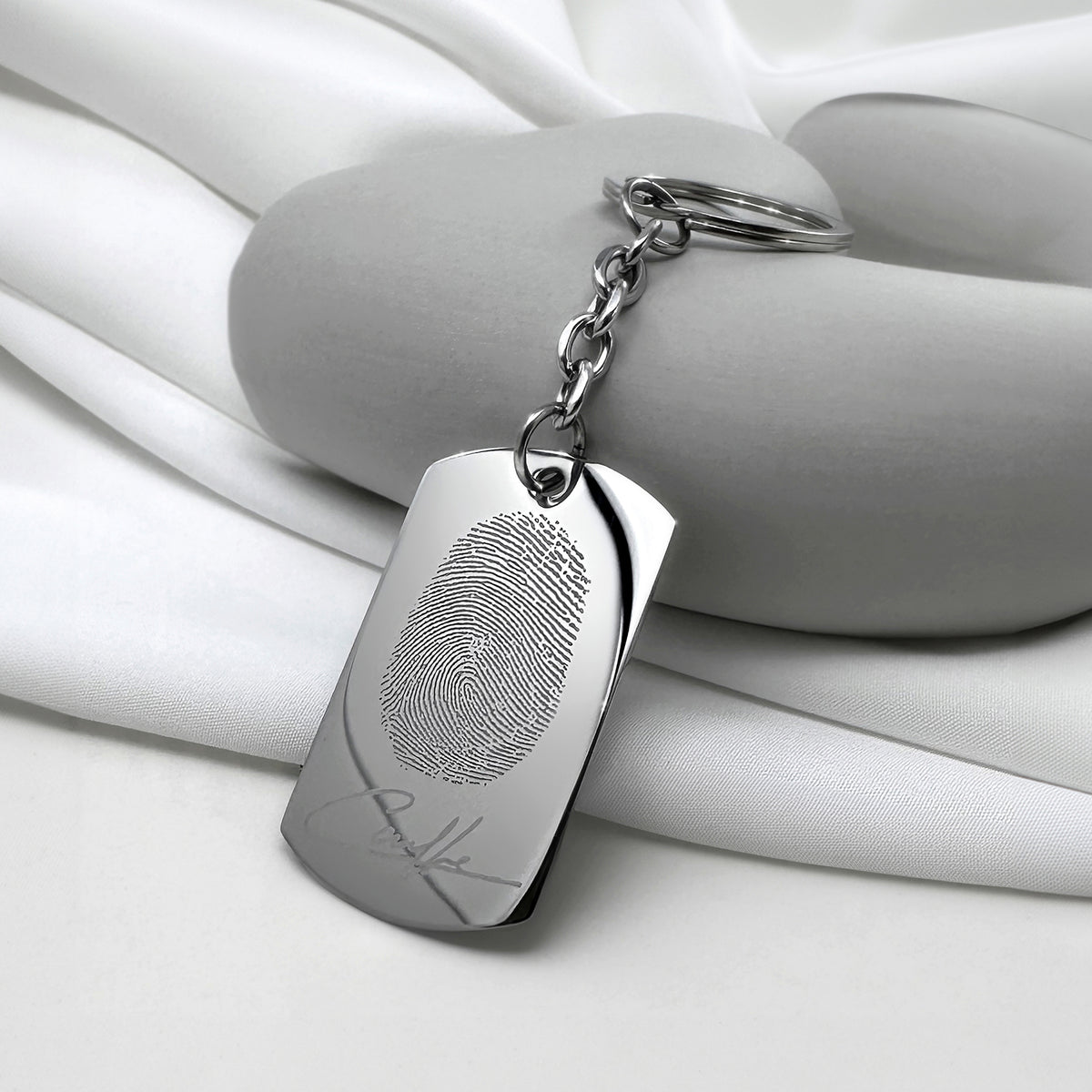 Personalized fingerprint dog tag keychain displayed in a styled setting with custom fingerprint and signature engraving