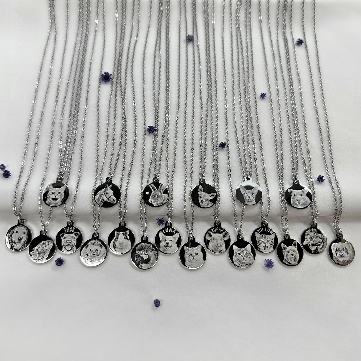 Multiple silver necklaces with round engraved pendants are arranged in rows on a white background. Each pendant features a different personalized pet portrait, including a cat, rabbit, dog, duck, duckling, ferret, bearded dragon, chicken, parrot, hedgehog, hamster, lizard and fish.