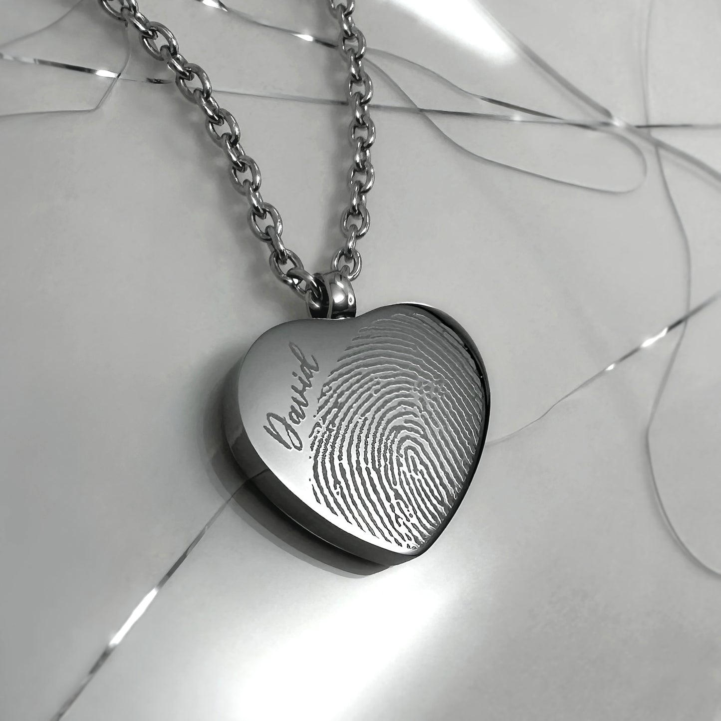 Close-up of a polished stainless-steel heart urn necklace engraved with a fingerprint.