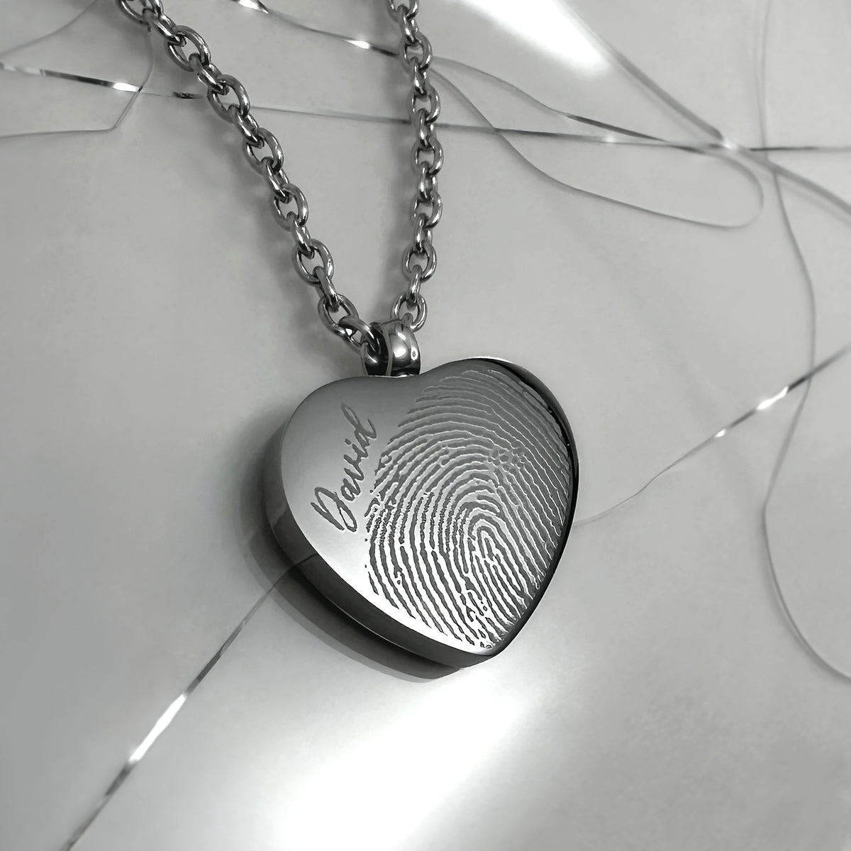 Close-up of a polished stainless-steel heart urn necklace engraved with a fingerprint.