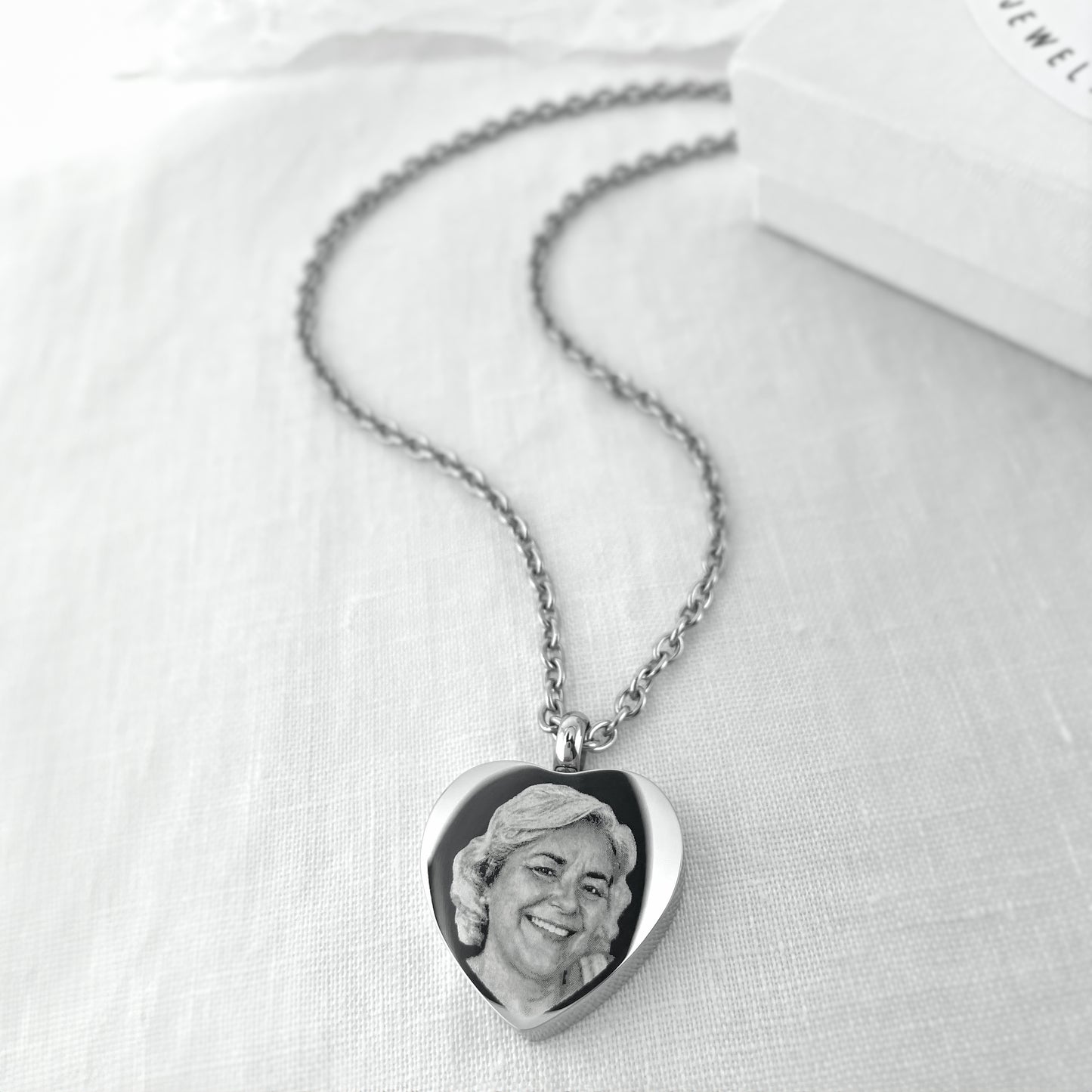 Heart-shaped cremation urn necklace engraved with a custom portrait and displayed on a silver chain.