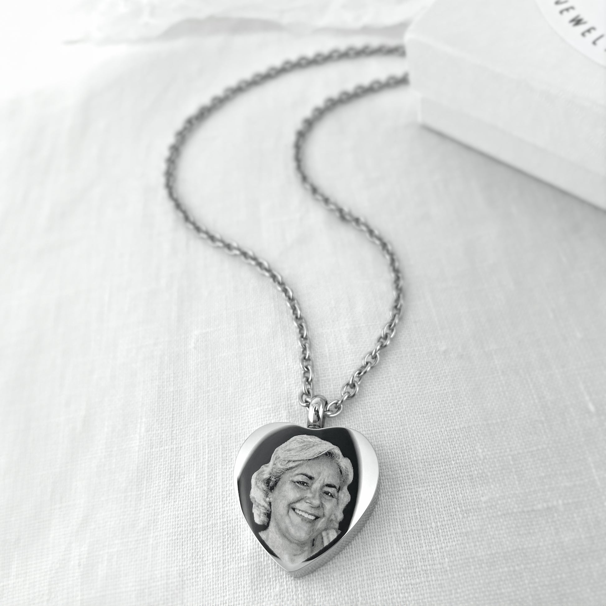 Heart-shaped cremation urn necklace engraved with a custom portrait and displayed on a silver chain.