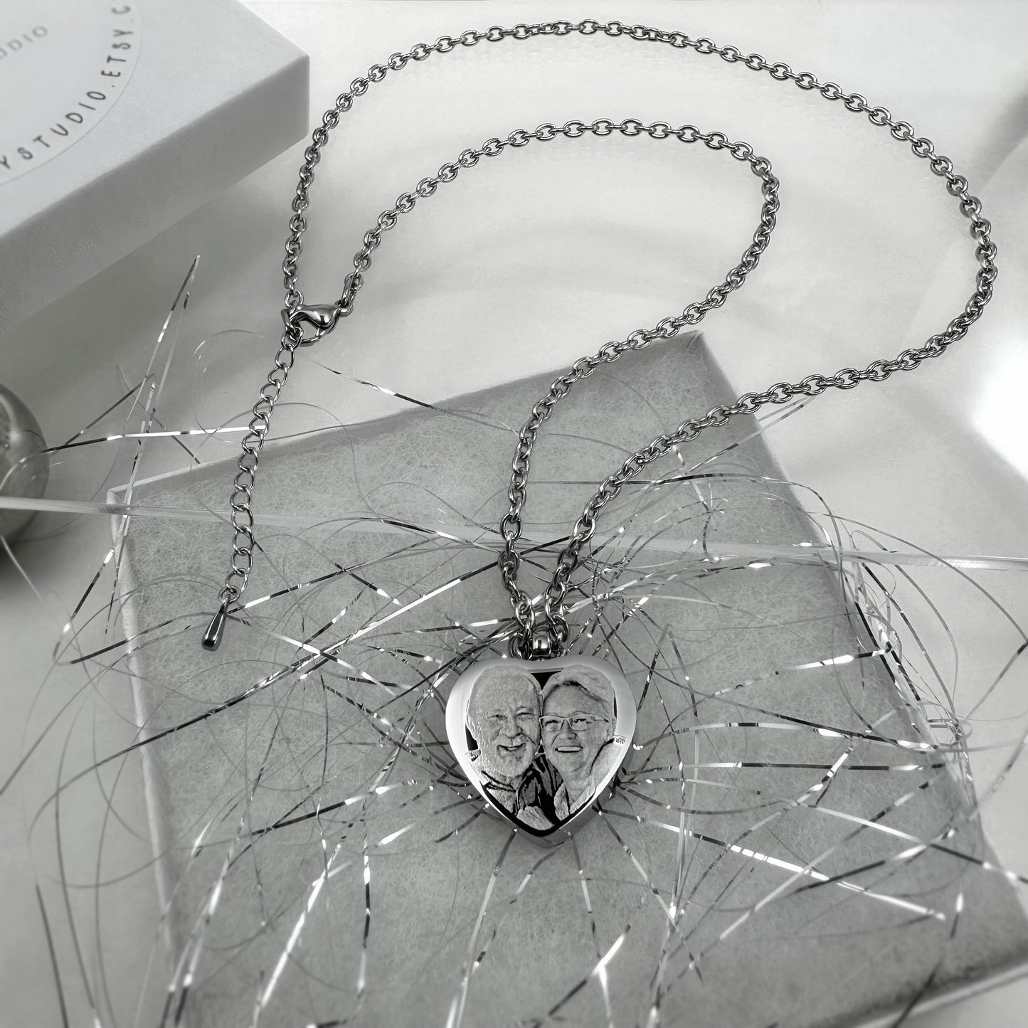 Heart-shaped cremation urn necklace engraved with a custom portrait and displayed on an ornamental surface.
