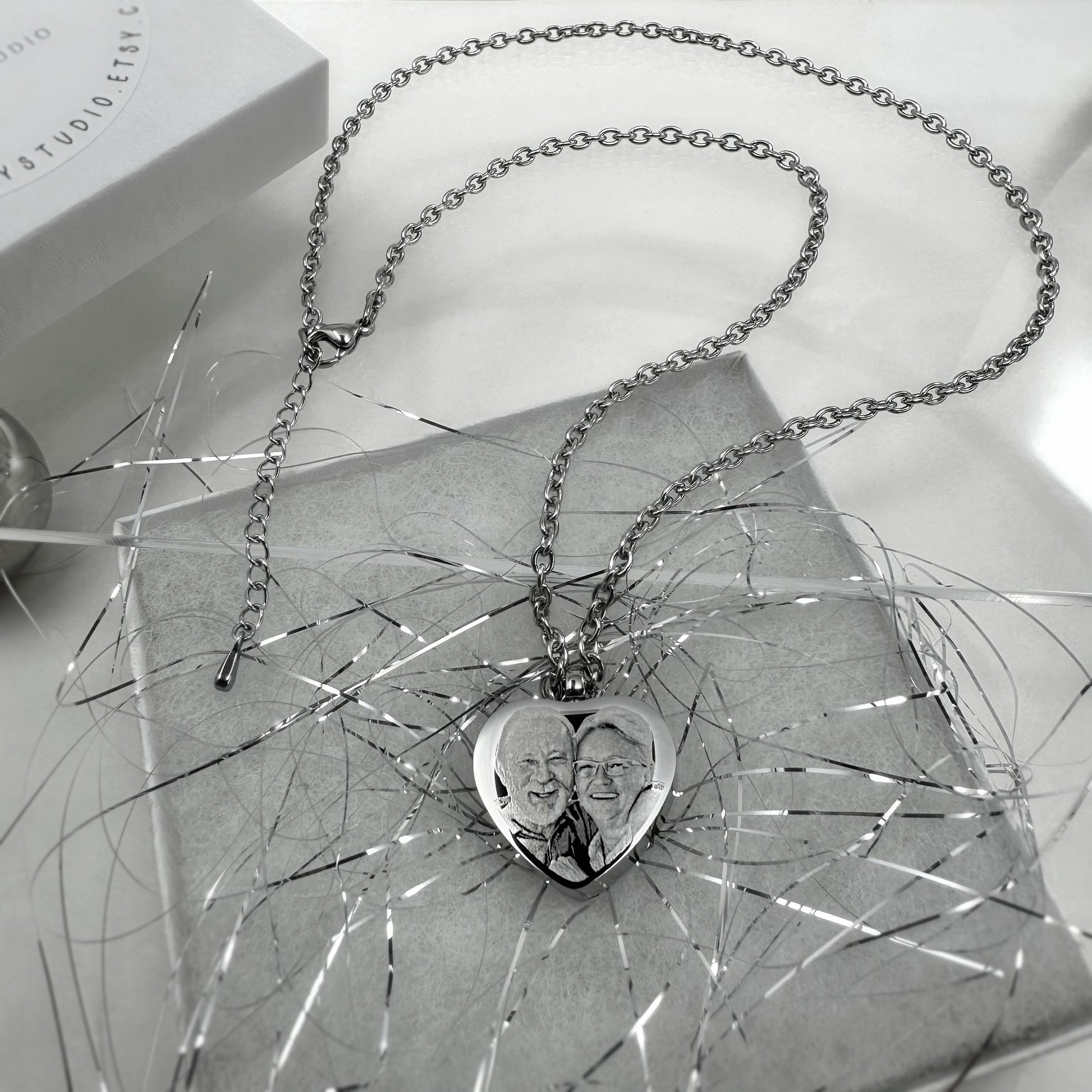 Heart-shaped cremation urn necklace engraved with a custom portrait and displayed on an ornamental surface.