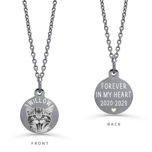 A view of a front and back of a round silver disc pendant necklace on a white background: the front shows an engraved cat portrait with a personalized pet name, and the back reads 'FOREVER IN MY HEART with custom dates with a heart. 