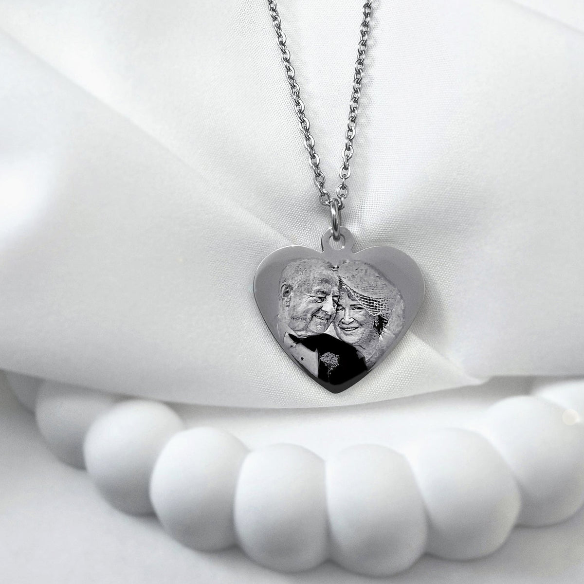 Personalized engraved couple photo heart necklace displayed on a soft neutral background with polished silver pendant