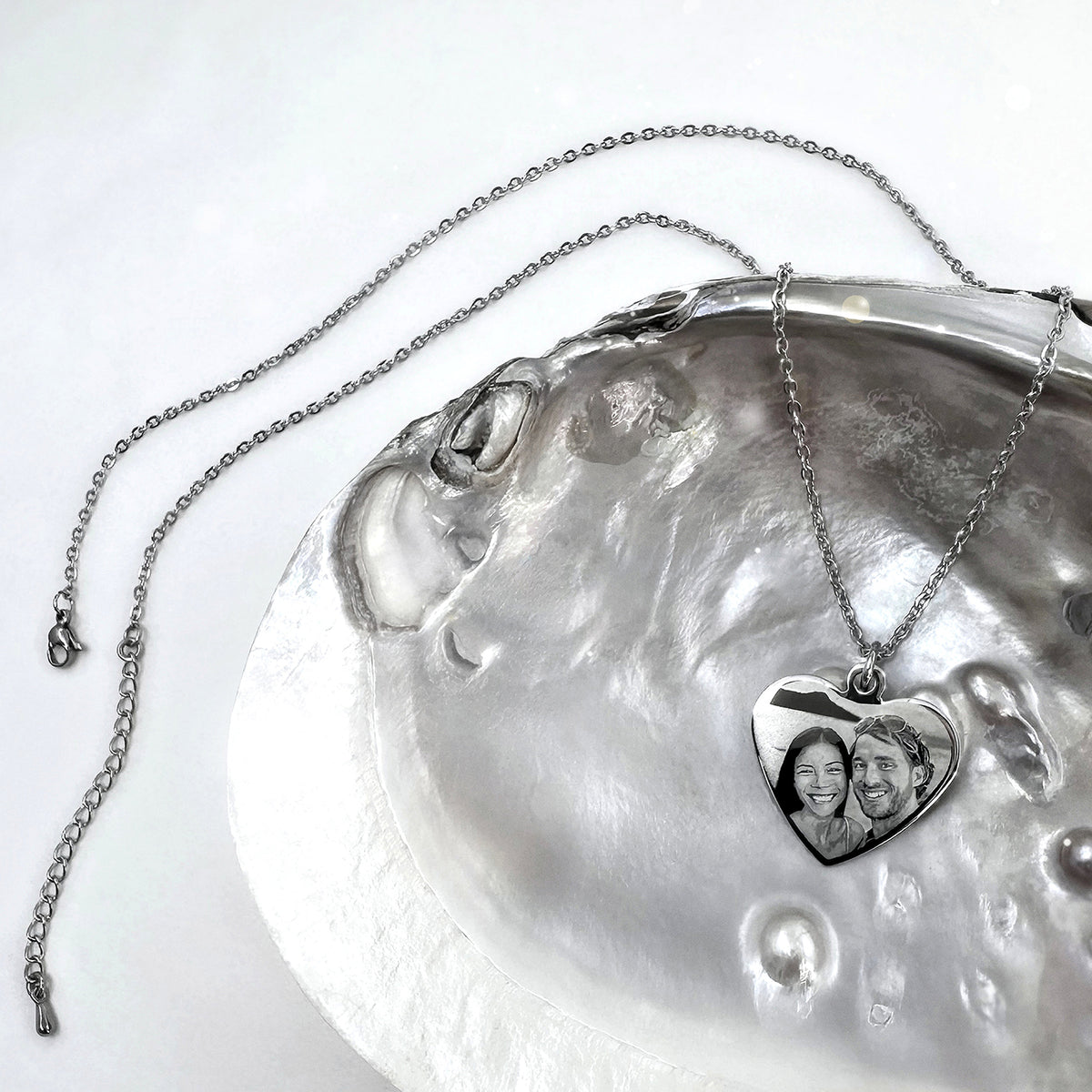 Personalized couple photo silver heart-shaped necklace displayed on a natural shell with polished stainless steel pendant and chain