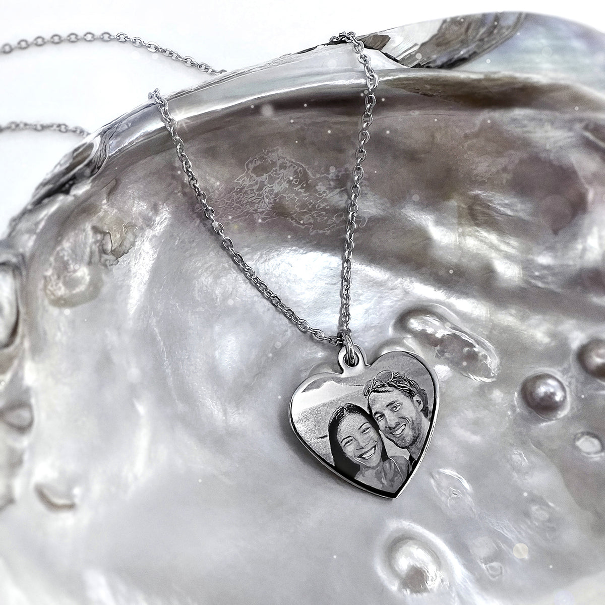 Personalized couple photo heart necklace displayed on a natural shell with polished stainless-steel pendant and chain