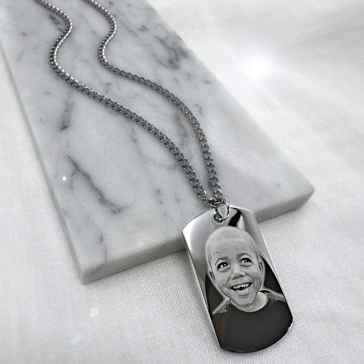 Personalized child portrait photo engraved on a small dog tag necklace displayed on a marble background