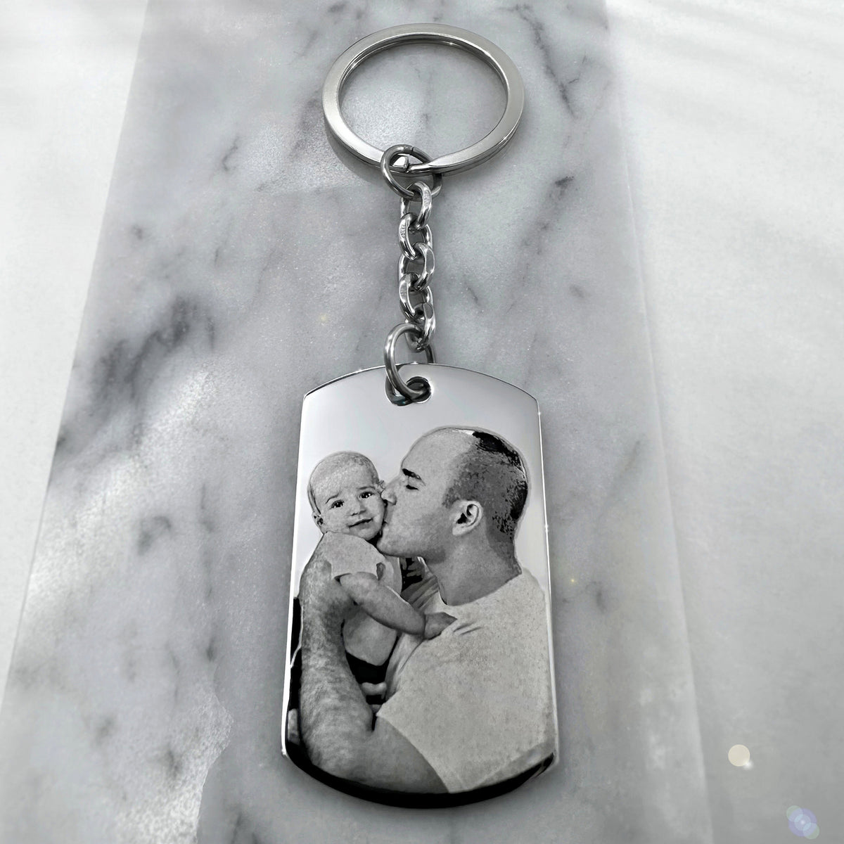 Personalized Father’s Day dog tag keychain with custom father and baby portrait engraving displayed on a marble background