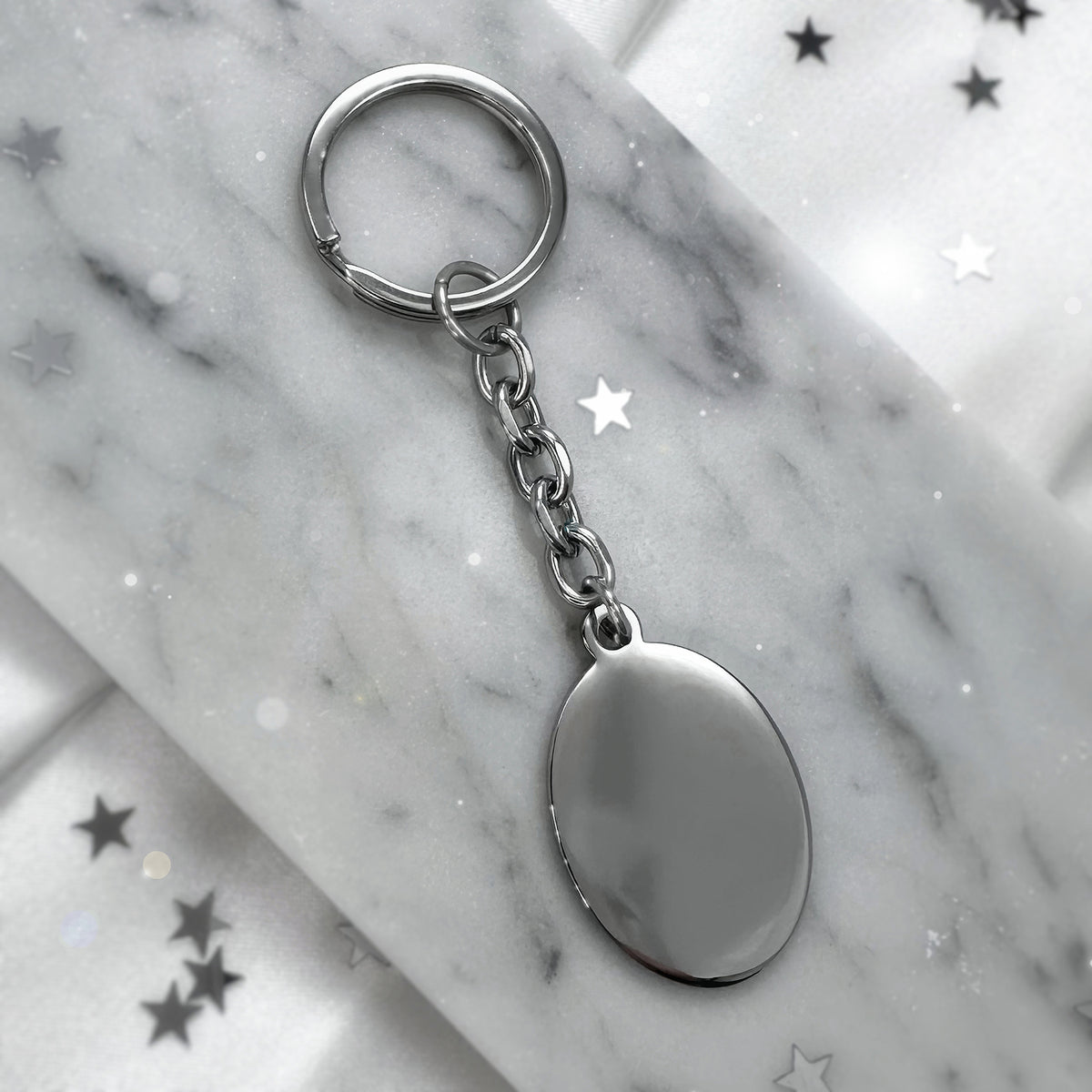 Blank polished oval stainless-steel keychain displayed on marble, ready for custom photo, fingerprint, handwriting, or message engraving