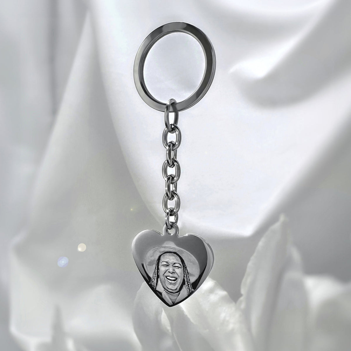 Personalized memorial silver heart keychain with custom photo portrait engraving displayed on soft satin