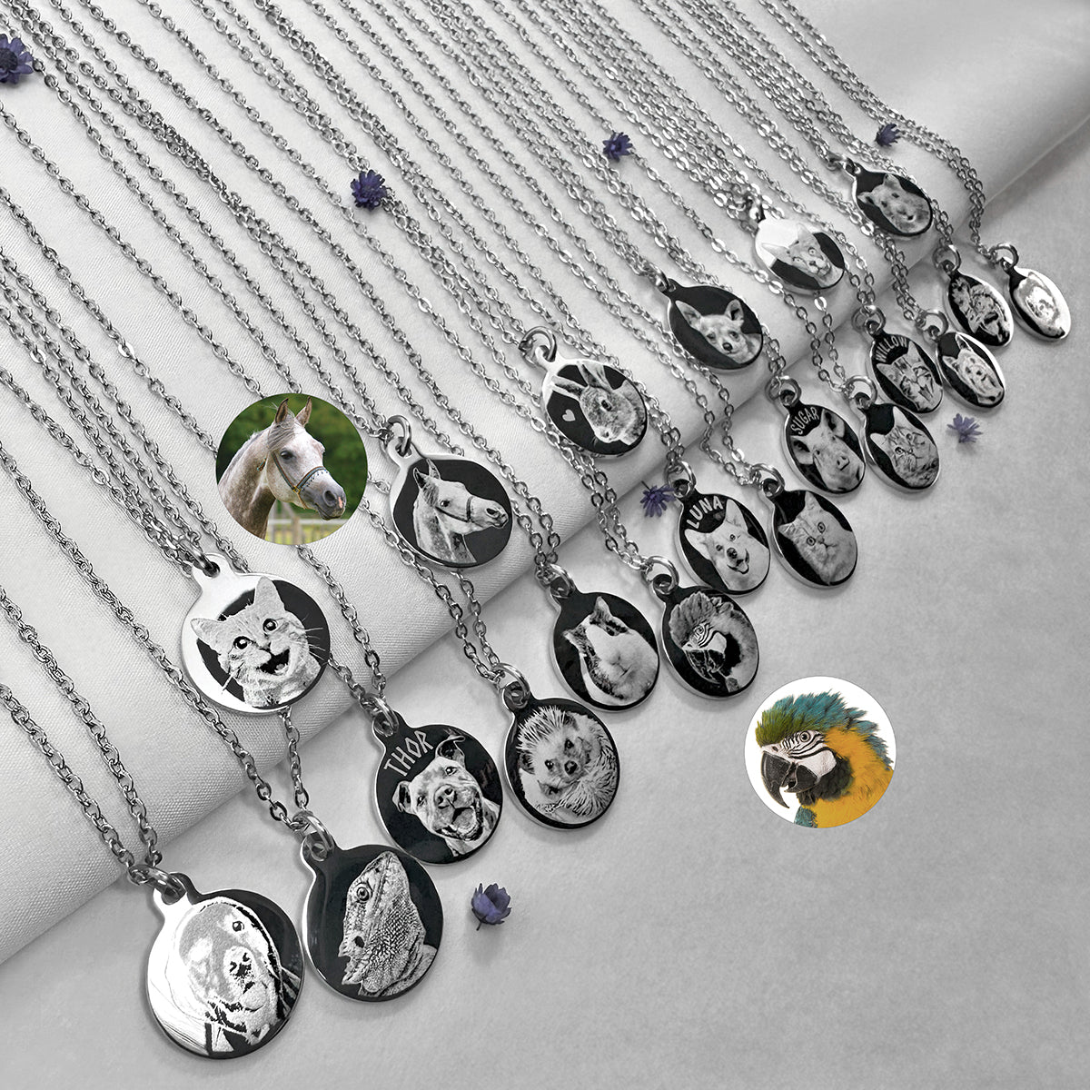 A set of silver chain necklaces with round pendants, each engraved with a different custom animal or pet portrait, arranged diagonally on a light gray fabric background.