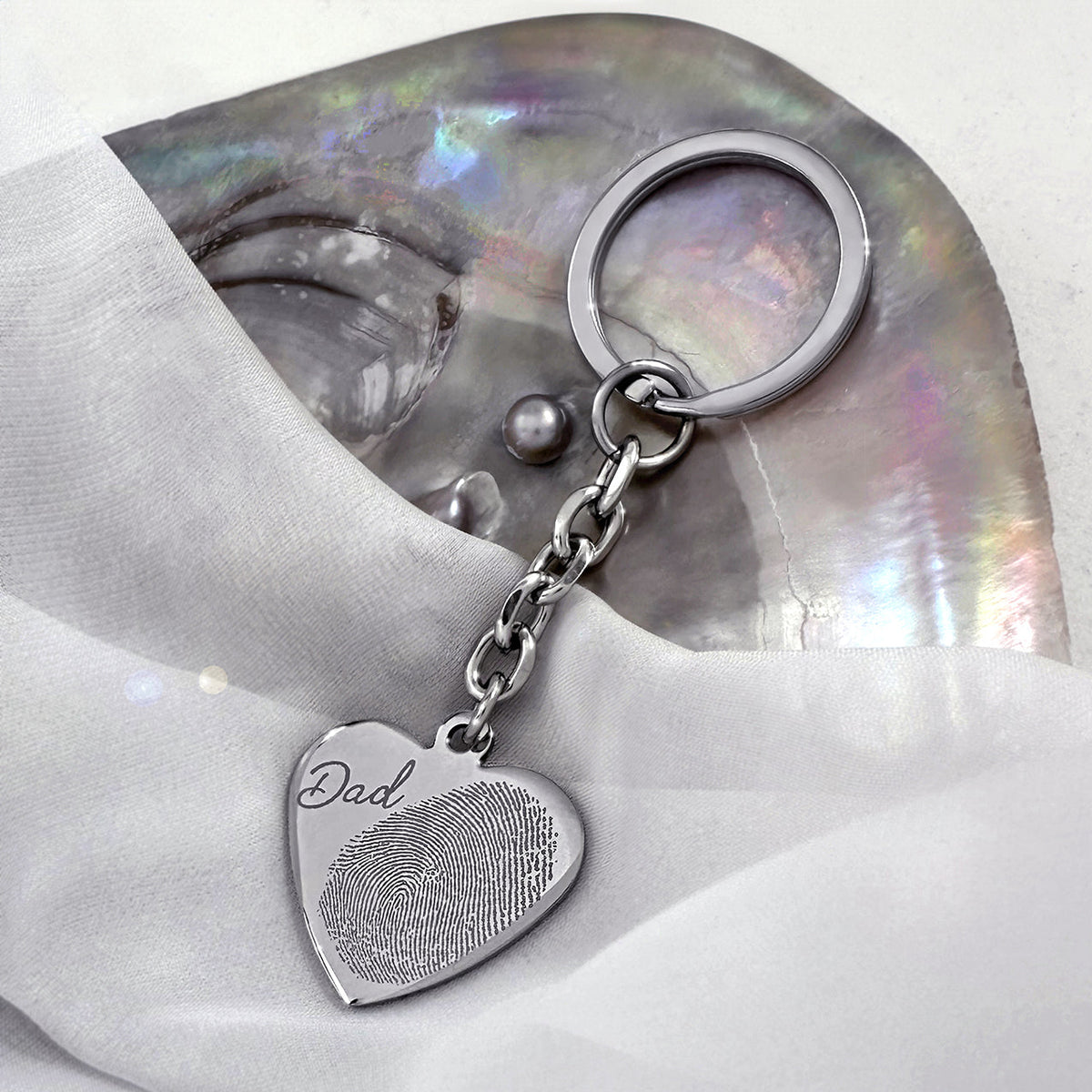 Personalized heart keychain with custom fingerprint engraving and handwriting "Dad" displayed on a white pearl dish