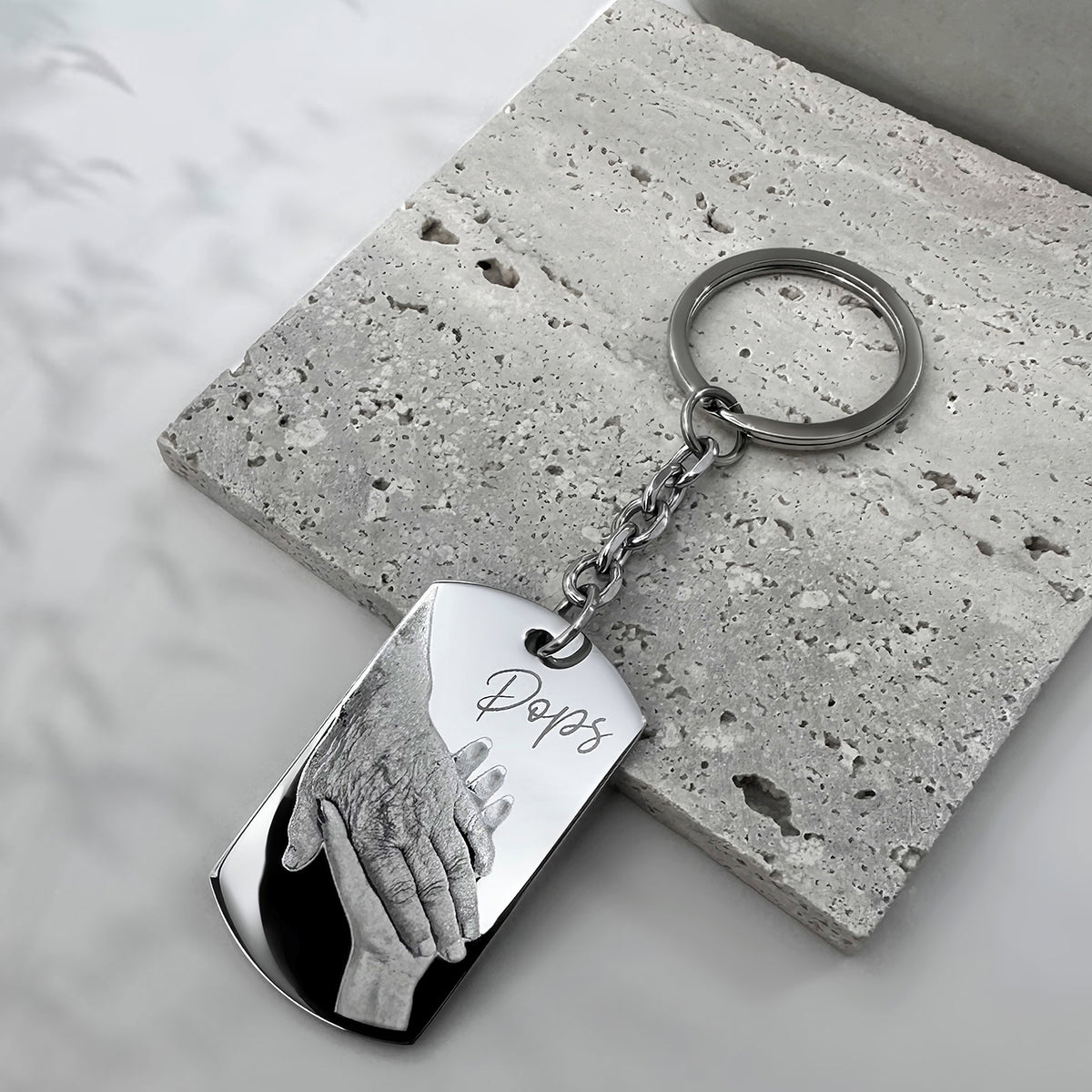Custom handprint memorial dog tag keychain engraved with “Pops” displayed on a textured stone background