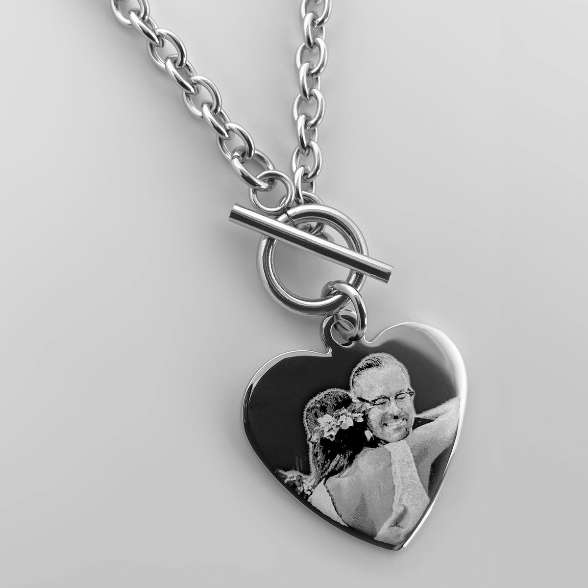 A silver heart-shaped pendant toggle clasp necklace engraved with a personalized wedding photo of a father and a daughter.