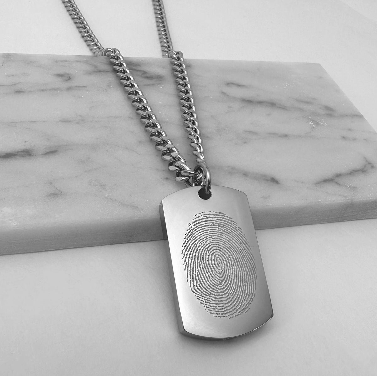 Custom engraved fingerprint dog tag urn necklace displayed on a marble background