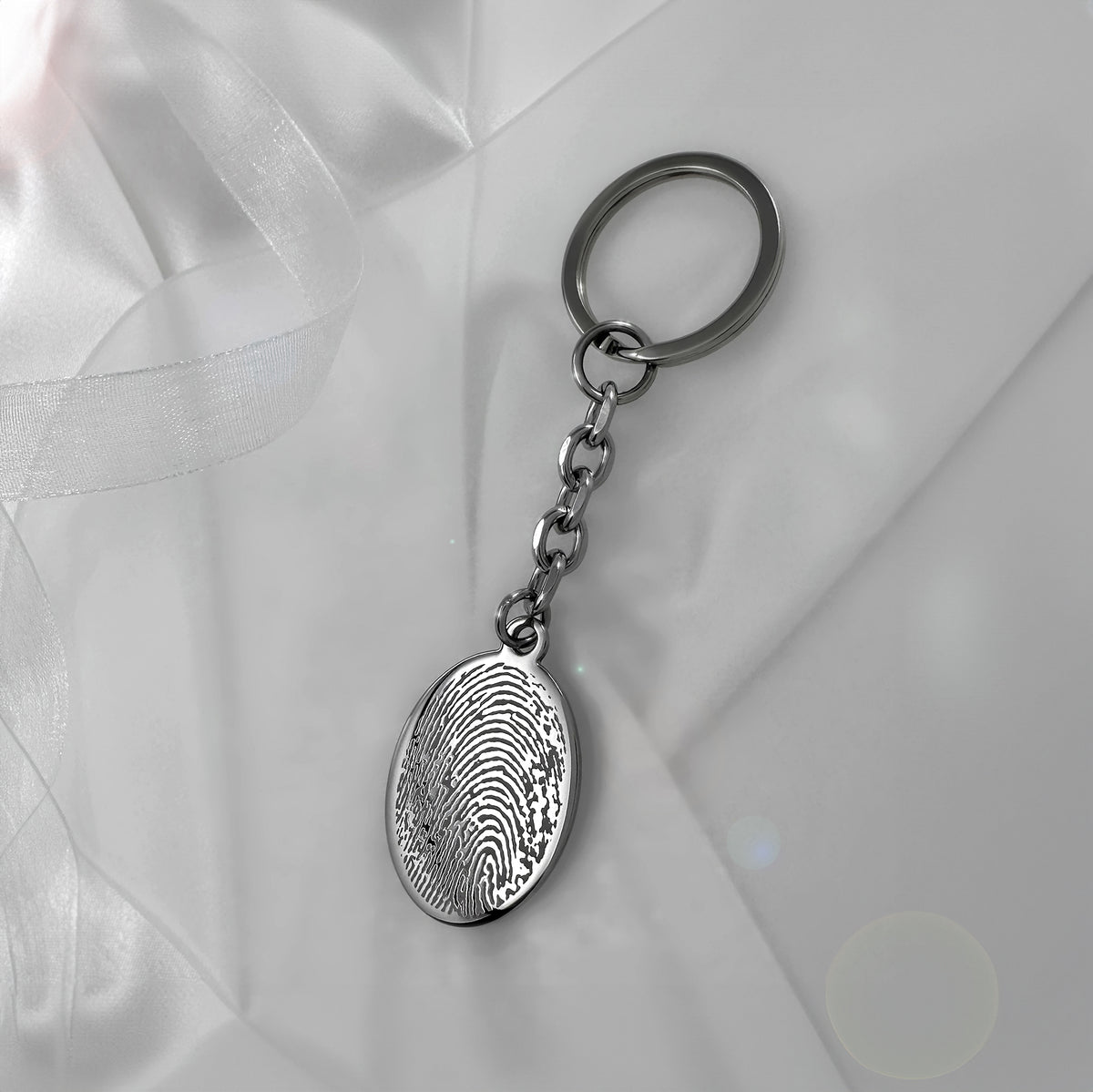 Actual fingerprint memorial oval keychain displayed on soft fabric with custom engraving