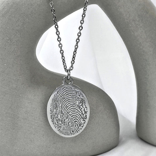 Personalized engraved silver fingerprint oval necklace displayed in a modern styled stand