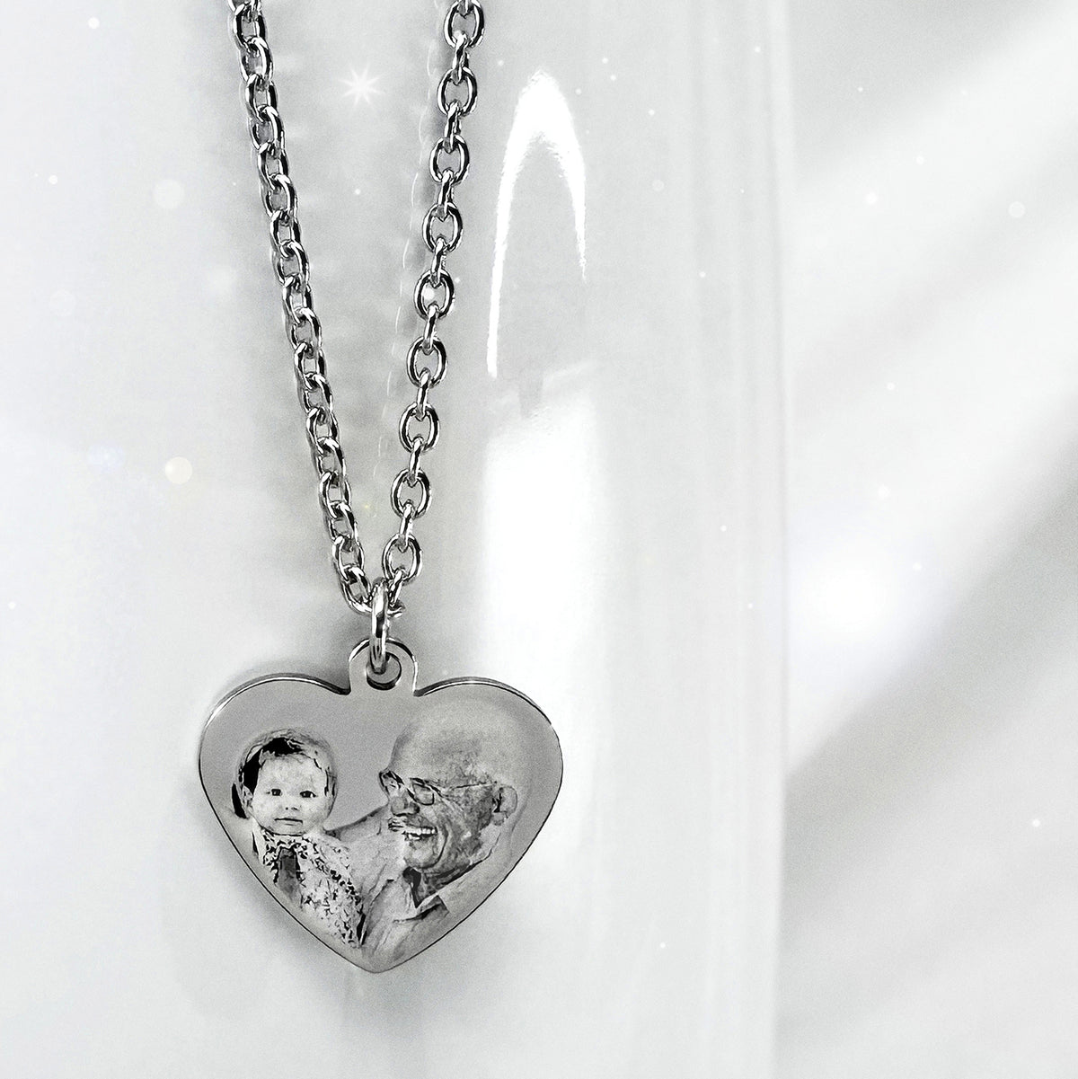 A silver heart-shaped pendant necklace featuring a custom photo engraving of a grandfather and a granddaughter, displayed on a white background.