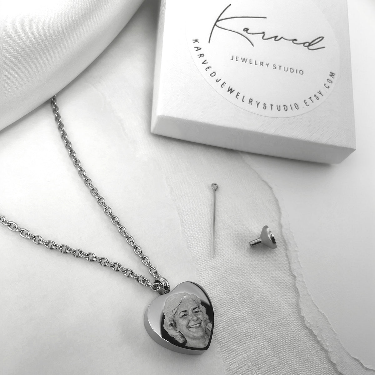 Heart cremation necklace engraved with a portrait and displayed beside urn filling tools and gift box