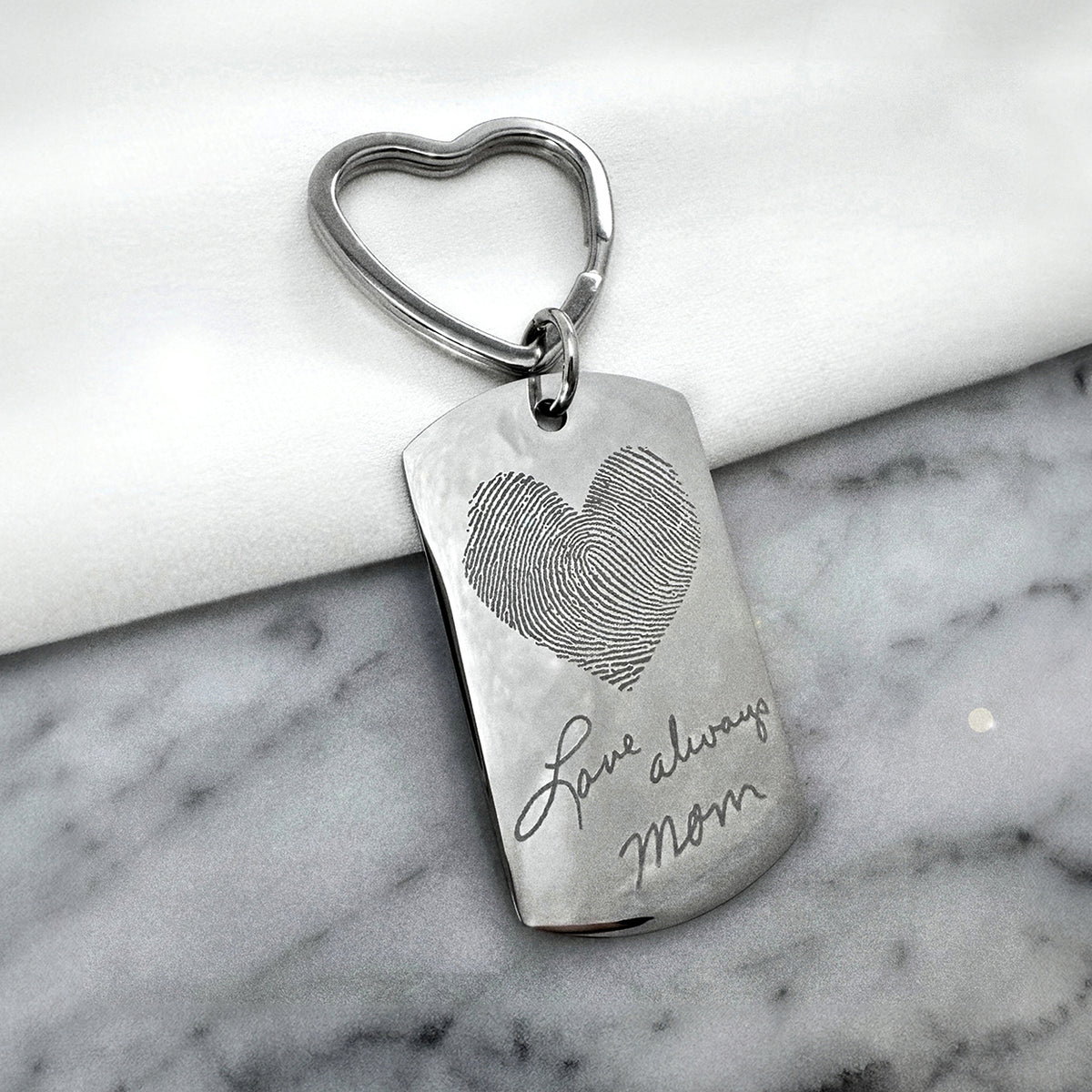 Custom heart-shaped fingerprint dog tag keychain with heart keyring displayed on marble, engraved with a personalized name and message