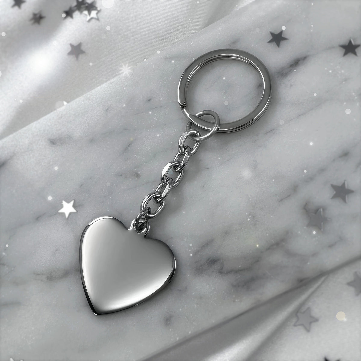 A silver blank heart-shaped keychain, resting on a grey marble slab, ready for engraving
