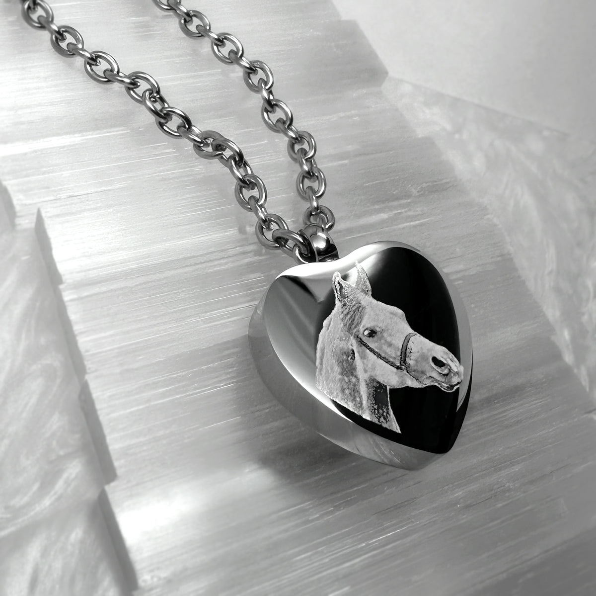 A stainless-steel heart-shaped cremation urn pendant necklace featuring an engraved horse head portrait design.