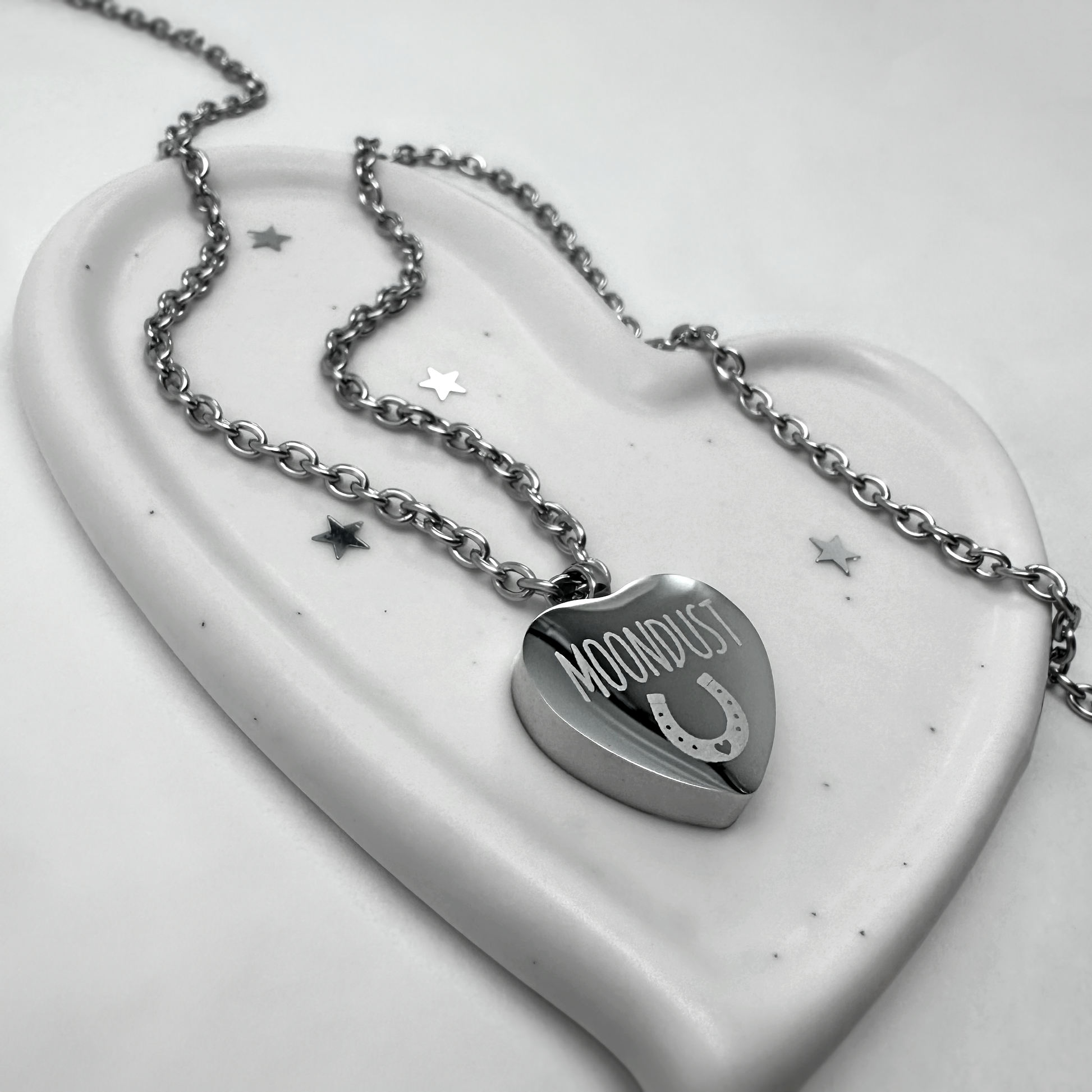 Heart-shaped horse cremation urn necklace engraved with the name “Moondust” and a horseshoe on polished stainless steel.