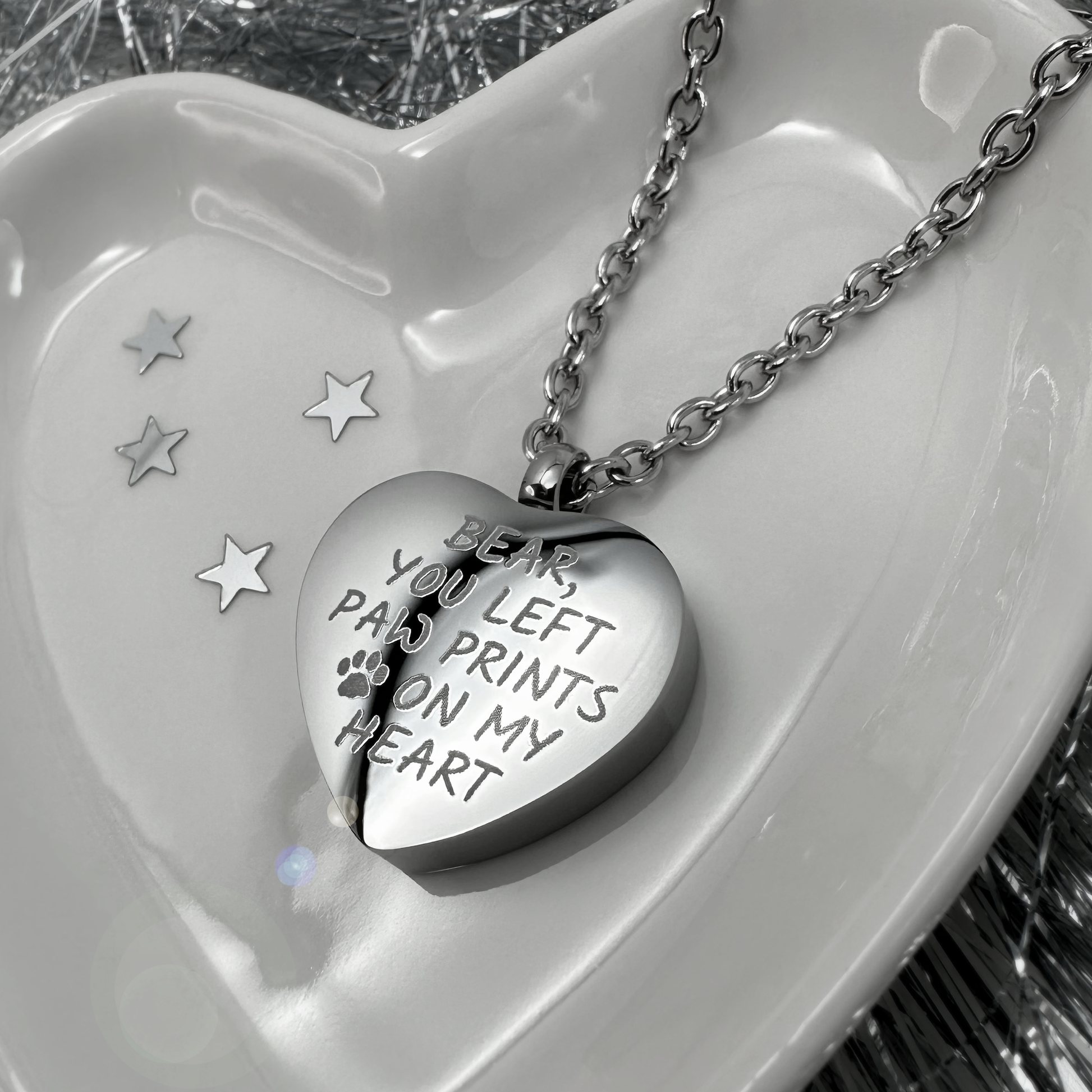 Heart-shaped pet cremation urn necklace engraved with the memorial message “Bear, you left paw prints on my heart” on polished stainless steel.