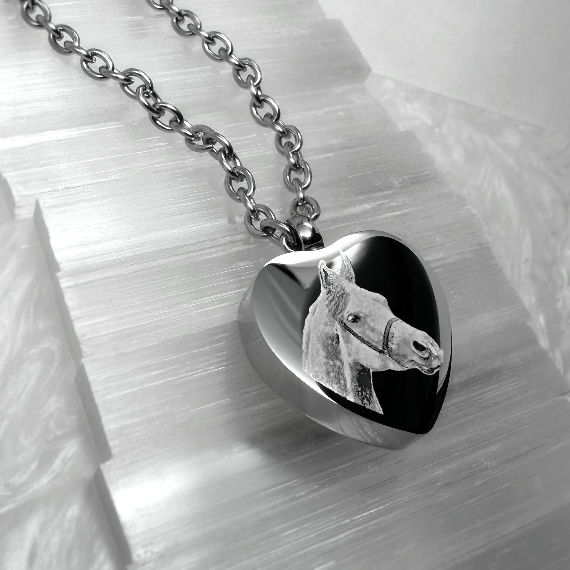 Close-up of a heart-shaped horse cremation urn necklace engraved from a custom horse photo.