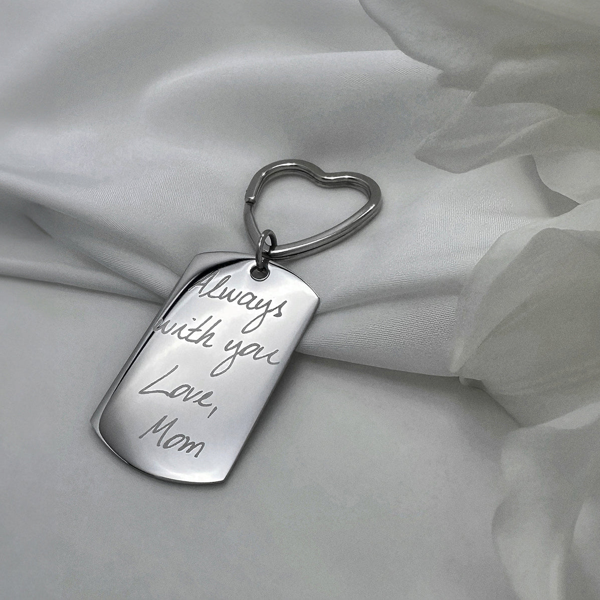 Handwriting dog tag keychain with heart-shaped keyring engraved “Always with you, Love, Mom” in a soft lifestyle setting