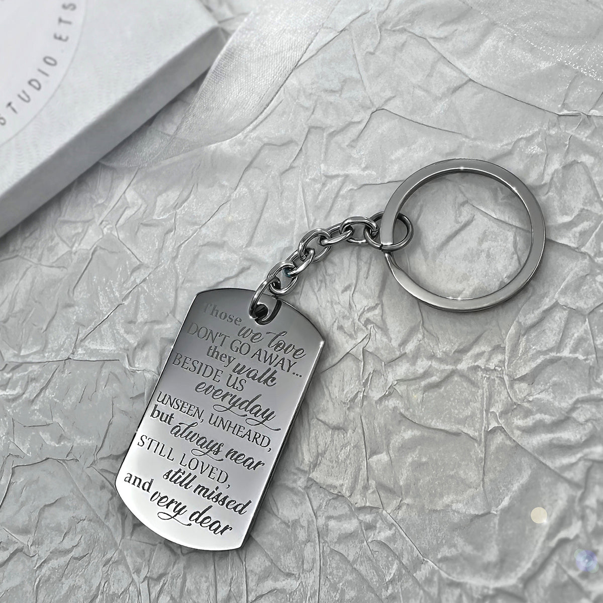 Memorial dog tag keychain close-up engraved with “Those we love don’t go away, they walk beside us every day” remembrance message