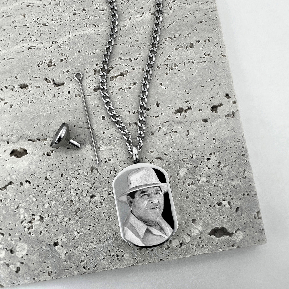 Custom photo engraved on a small dog tag urn necklace displayed on a textured neutral background
