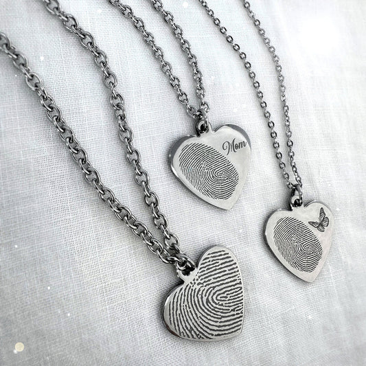 Three silver heart-shaped fingerprint pendant necklaces engraved with an actual custom fingerprint, 'Mom' and a small butterfly design.