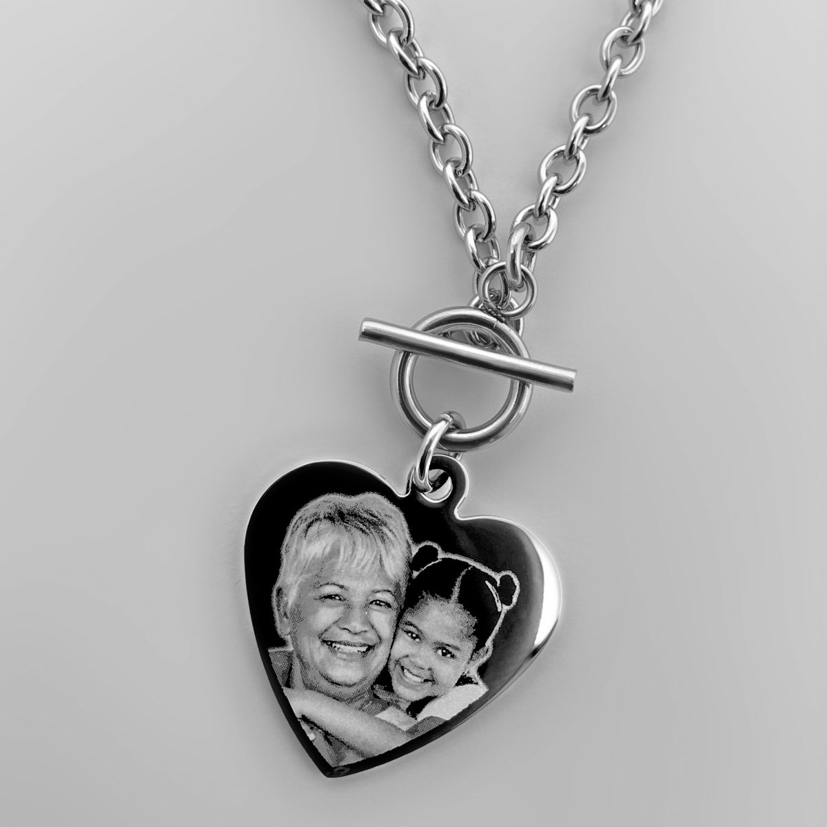 A silver heart-shaped pendant with toggle clasp chain featuring a custom memorial photo of grandma and granddaughter.