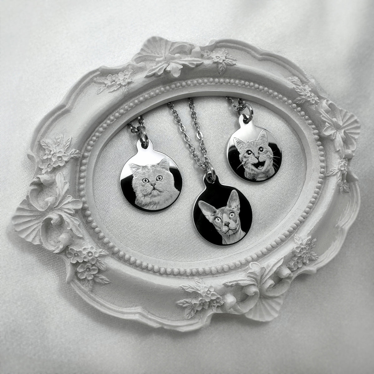 Three disc pendant necklaces engraved with personalized cat portraits displayed on an ornate white tray. 