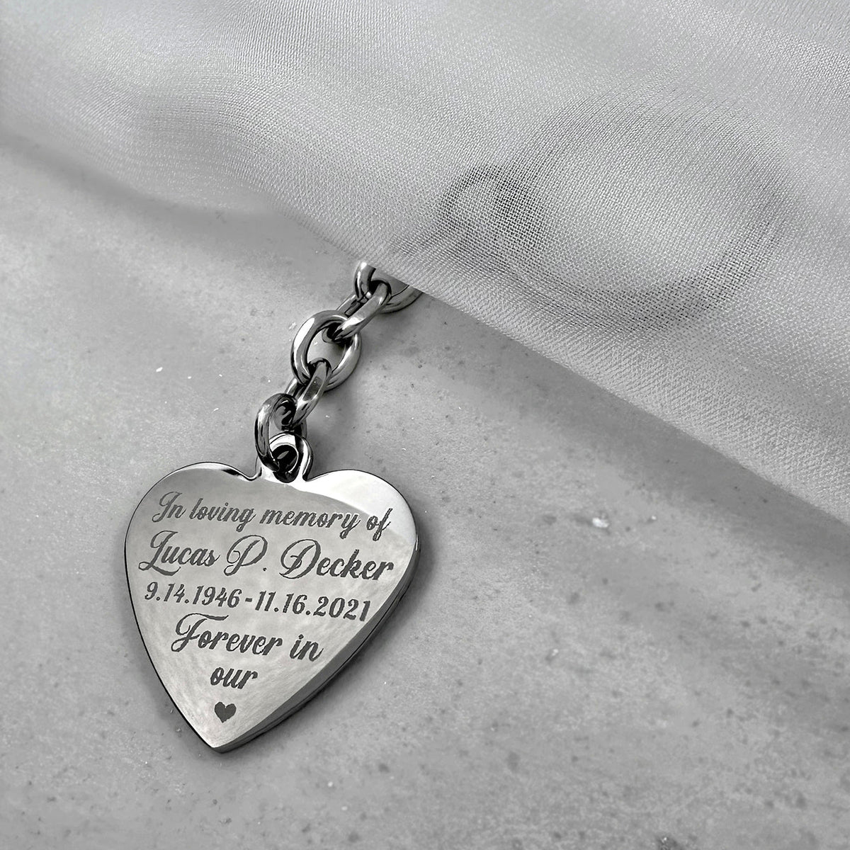 Personalized memorial heart keychain engraved with a loved one’s name, birth and memorial dates, and a custom “Forever in our heart” remembrance message