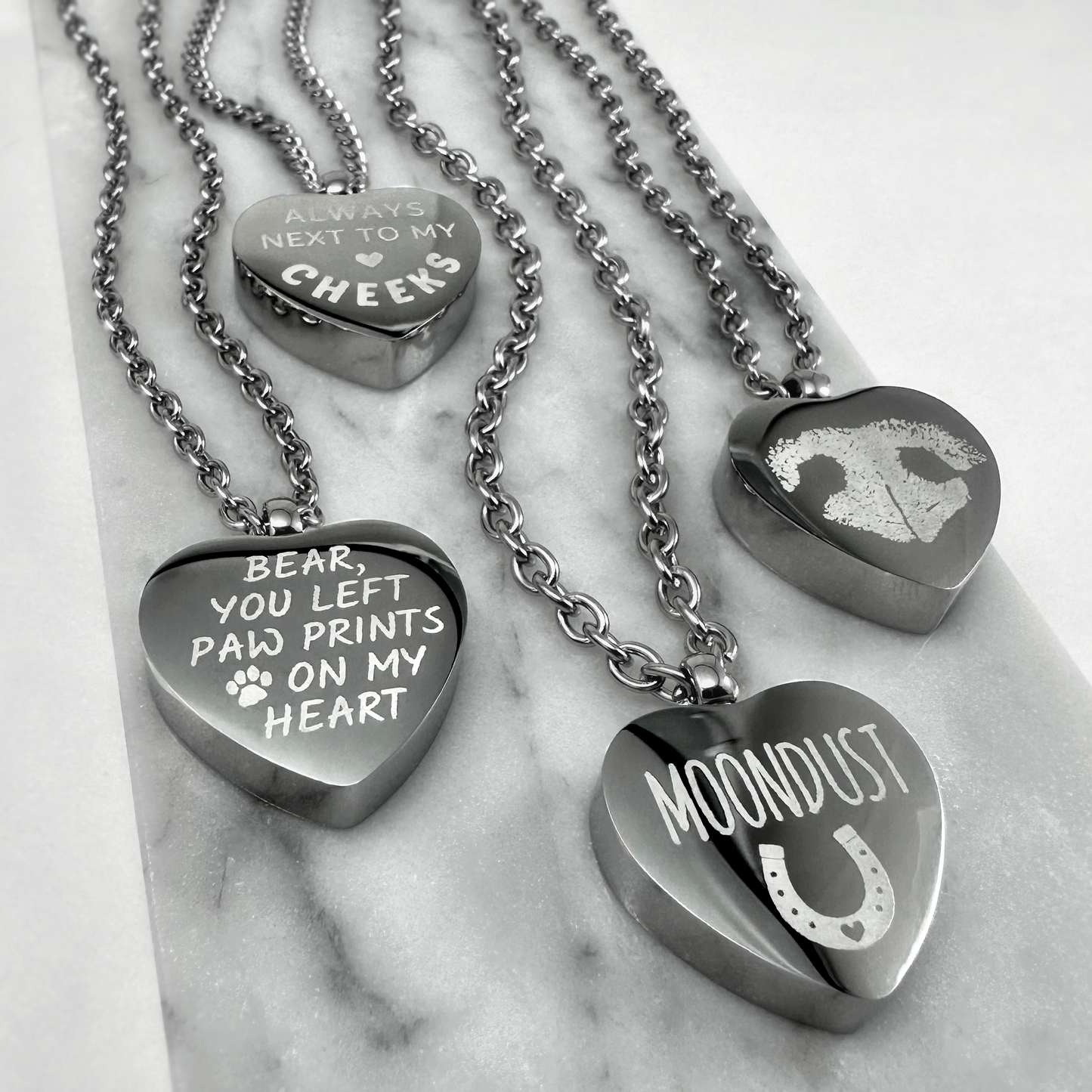 Heart-shaped pet memorial urn necklaces engraved with custom paw-print messages, a pet nose print, and a horse name with horseshoe design.