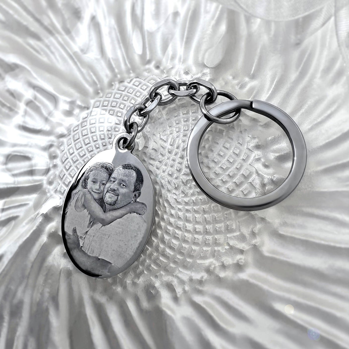 Personalized photo memorial oval keychain displayed on a glass dish with custom portrait engraving