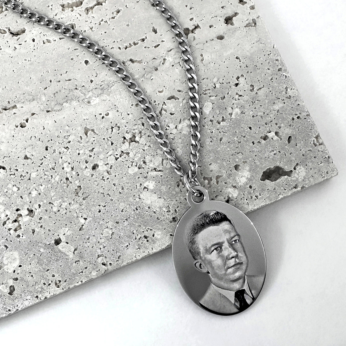 Custom portrait photo silver oval men's necklace displayed on a textured neutral background