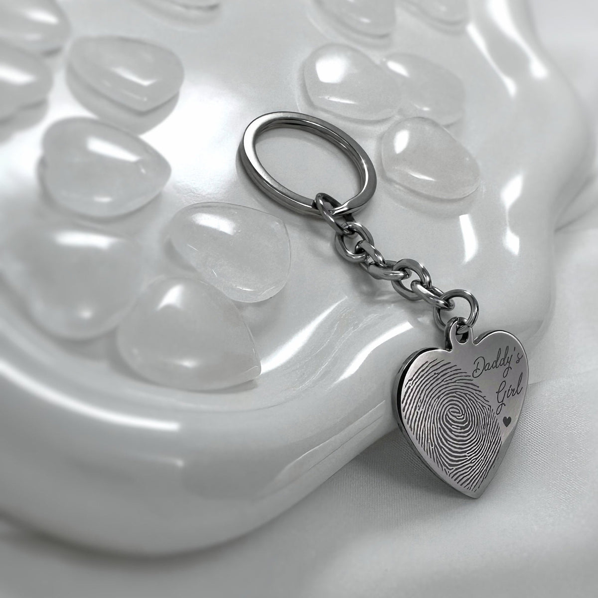 Personalized silver heart keychain with custom fingerprint and handwriting engraving displayed on a white glass dish
