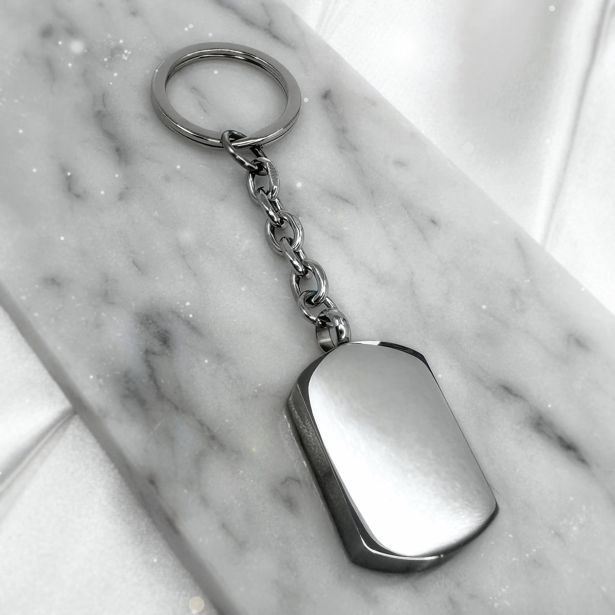 Blank polished stainless-steel dog tag urn keychain displayed on marble, ready for custom engraving